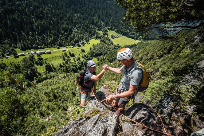 A climbing guide helping a climber up to the top of a cliff face.